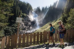 Zwei Frauen wandern am Wasserfall vorbei und bestaunen diesen